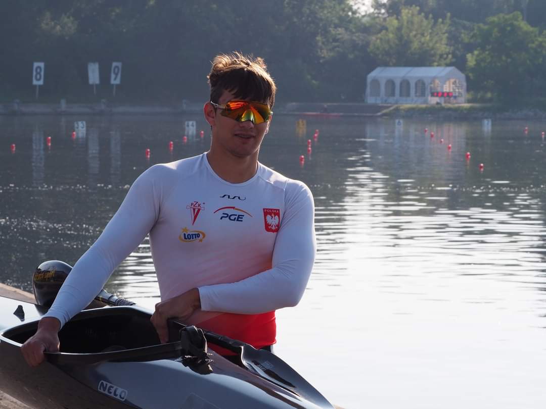 Kacper Kaszuba w stroju reprezentacji Polski przy kajaku na regatach